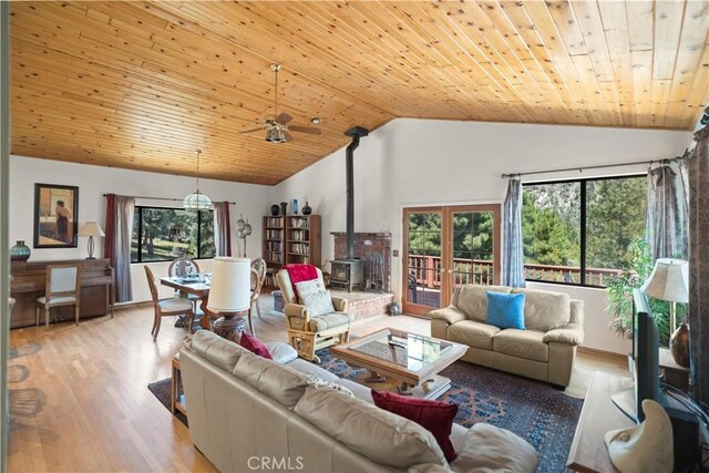 living area featuring plenty of natural light, a wood stove, a ceiling fan, and vaulted ceiling