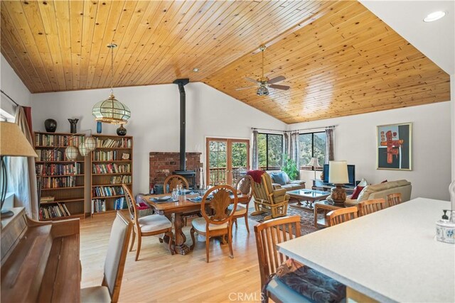 dining space with wood ceiling, a ceiling fan, a wood stove, and light wood-style flooring