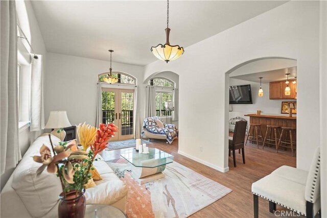 living room with bar, arched walkways, french doors, baseboards, and wood finished floors