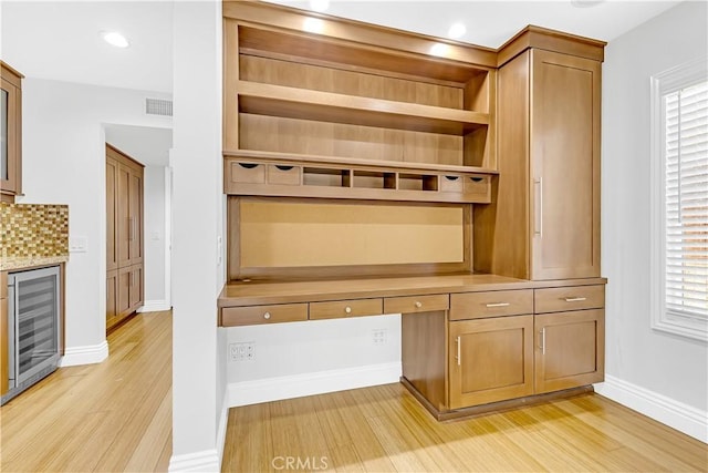 unfurnished office featuring built in desk, light wood-style flooring, a healthy amount of sunlight, wine cooler, and visible vents