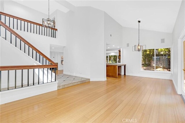 unfurnished living room featuring an inviting chandelier, stairs, light wood finished floors, and high vaulted ceiling