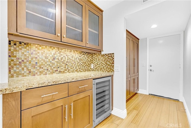 kitchen featuring glass insert cabinets, light stone counters, light wood finished floors, and beverage cooler