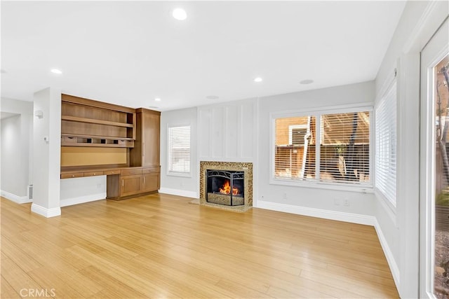 unfurnished living room with light wood-type flooring, recessed lighting, baseboards, and a premium fireplace
