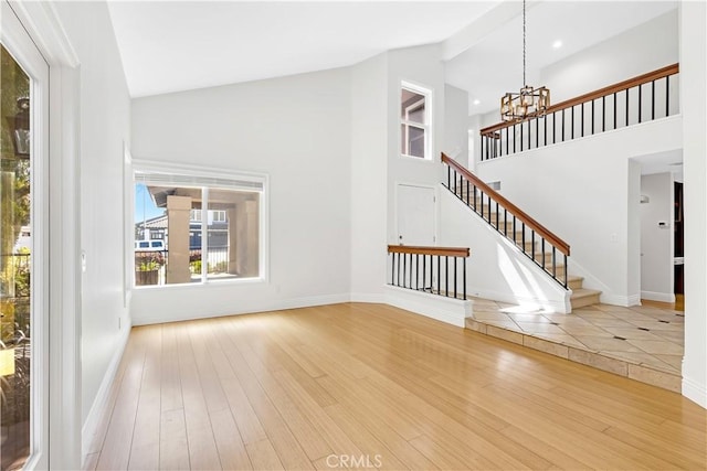 unfurnished living room featuring high vaulted ceiling, a notable chandelier, wood finished floors, and stairway