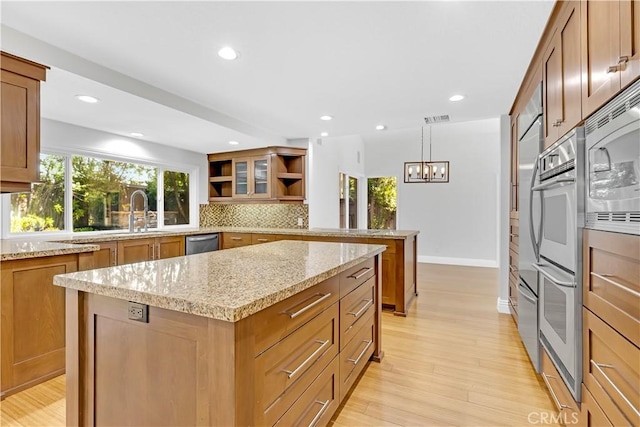 kitchen featuring brown cabinetry, open shelves, light stone countertops, backsplash, and stainless steel appliances