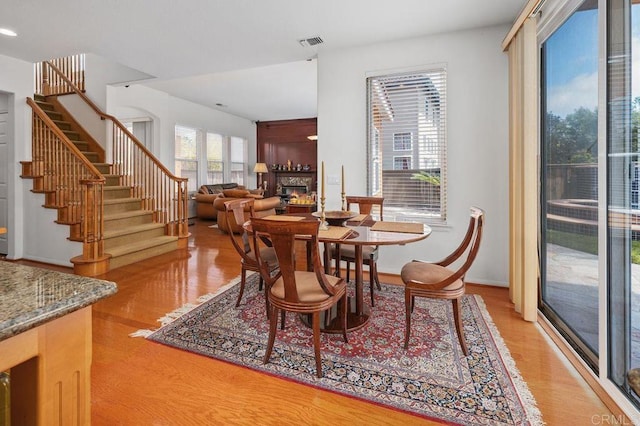 dining space featuring visible vents, stairs, light wood finished floors, and a warm lit fireplace
