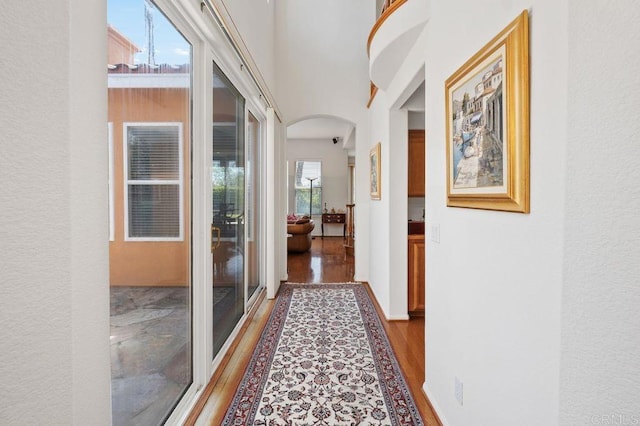 corridor with arched walkways, a textured wall, and wood finished floors