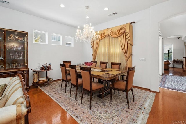 dining room featuring arched walkways, a chandelier, wood finished floors, and visible vents