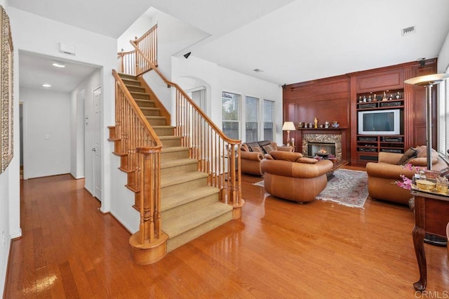 staircase with visible vents, recessed lighting, wood finished floors, and a lit fireplace