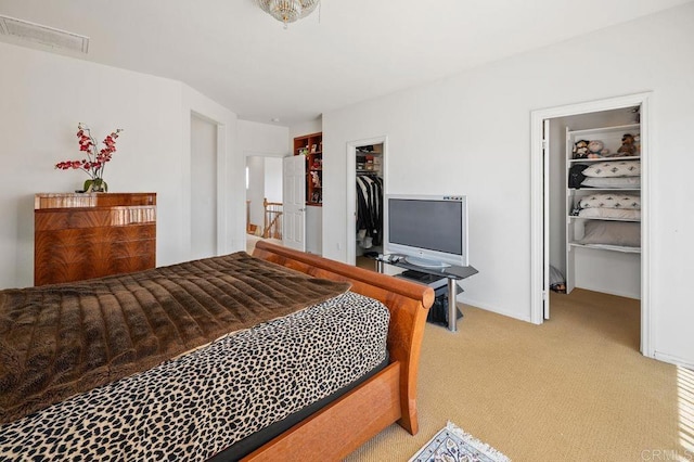 bedroom with a walk in closet, visible vents, baseboards, a closet, and light carpet