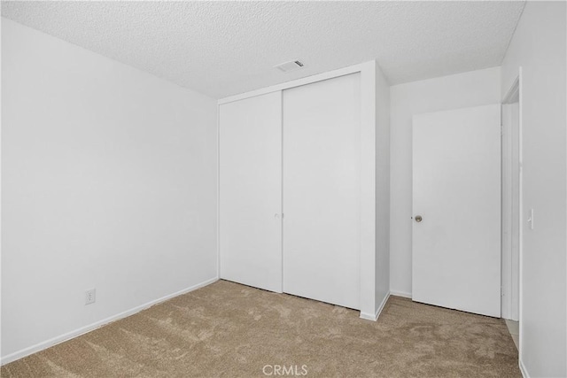 unfurnished bedroom featuring carpet flooring, a textured ceiling, baseboards, visible vents, and a closet