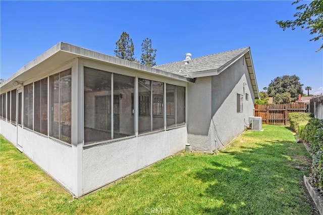 back of house featuring a sunroom, fence, a yard, a shingled roof, and stucco siding