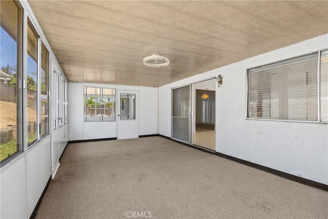 unfurnished sunroom featuring baseboards, carpet, and wood ceiling