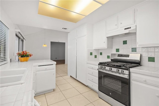 kitchen featuring a sink, stainless steel range with gas cooktop, tile countertops, under cabinet range hood, and visible vents