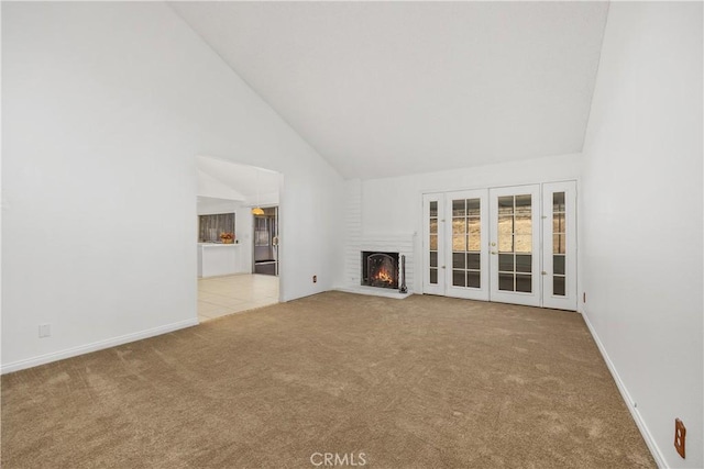 unfurnished living room featuring carpet floors, a fireplace, baseboards, high vaulted ceiling, and french doors