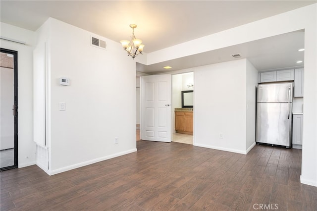 unfurnished living room featuring visible vents, dark wood-style flooring, baseboards, and an inviting chandelier