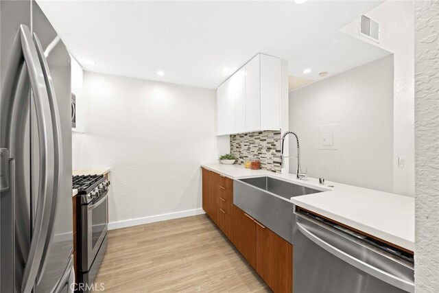 1310 N Detroit St Unit 405, Los Angeles, CA 90046 - kitchen featuring decorative backsplash, white cabinetry, a sink, light wood-style flooring, and stainless steel appliances