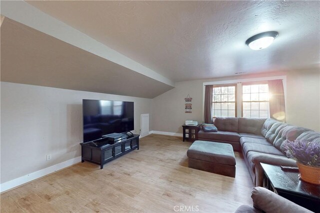 living room with a textured ceiling, baseboards, light wood-style flooring, and lofted ceiling