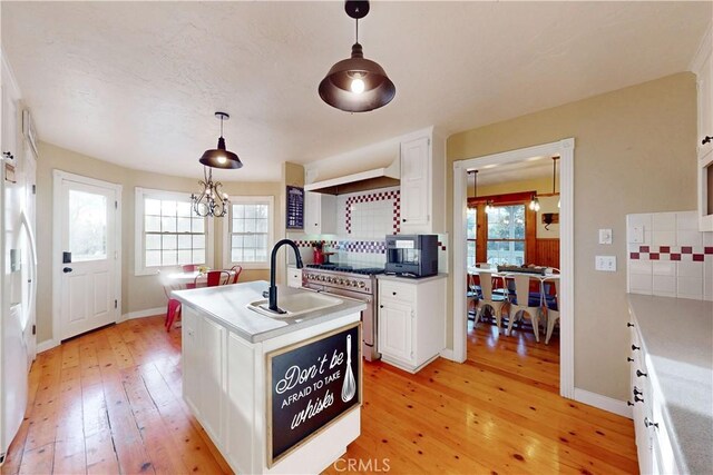 kitchen featuring high end stainless steel range, light wood-type flooring, white cabinets, a sink, and backsplash