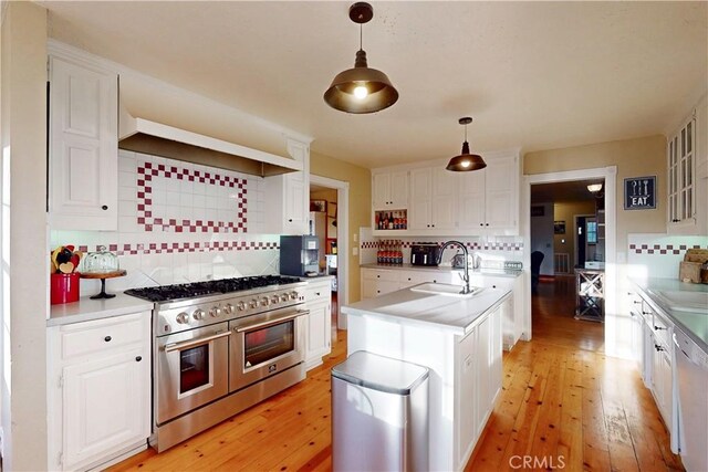 kitchen featuring a kitchen island with sink, backsplash, double oven range, light wood-type flooring, and a sink