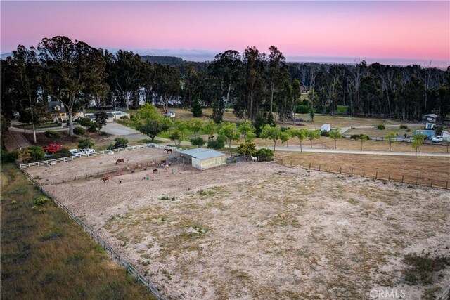 yard at dusk with an enclosed area, fence, and a view of trees