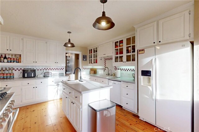 kitchen with a sink, light wood-style floors, backsplash, and white appliances