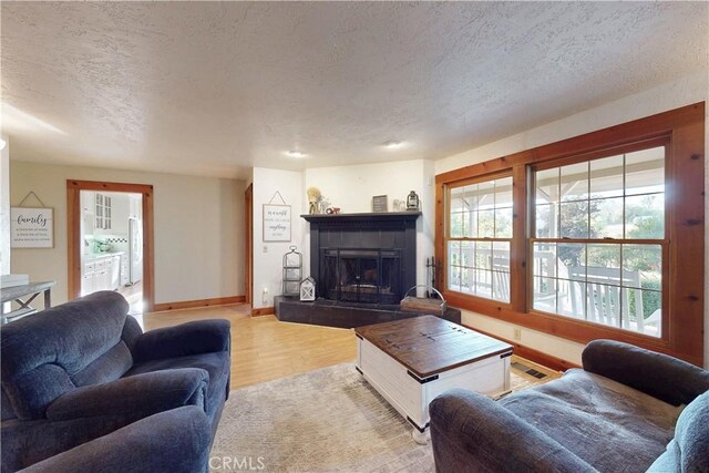 living room featuring a fireplace, a textured ceiling, light wood-style flooring, baseboards, and visible vents