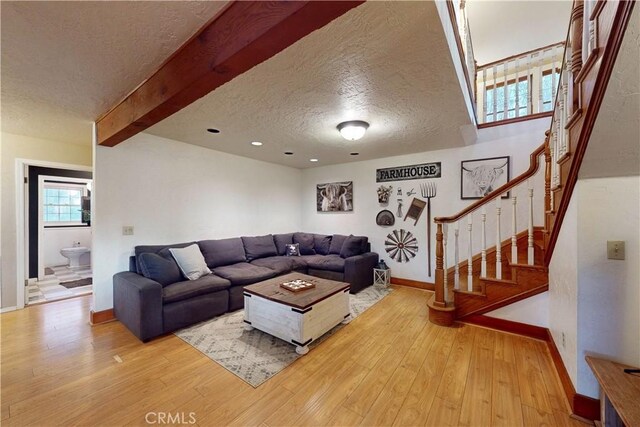 living room featuring baseboards, a textured ceiling, stairs, and light wood-style floors