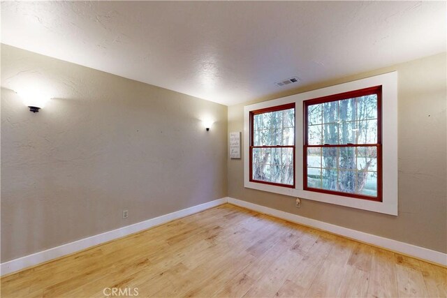 spare room featuring baseboards, wood finished floors, and visible vents