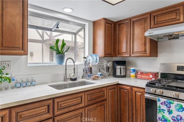 kitchen featuring under cabinet range hood, stainless steel gas range oven, brown cabinetry, and a sink