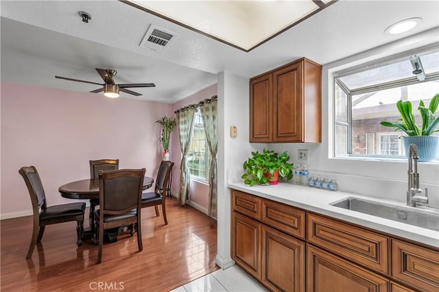 kitchen with brown cabinets, a ceiling fan, a sink, visible vents, and light countertops