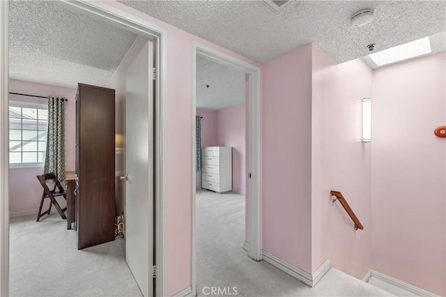 corridor featuring a skylight, a textured ceiling, an upstairs landing, carpet flooring, and baseboards