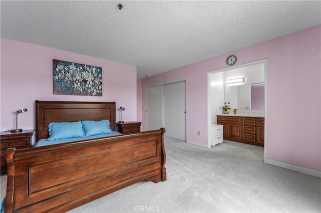 bedroom featuring a closet, a textured ceiling, ensuite bath, light carpet, and baseboards