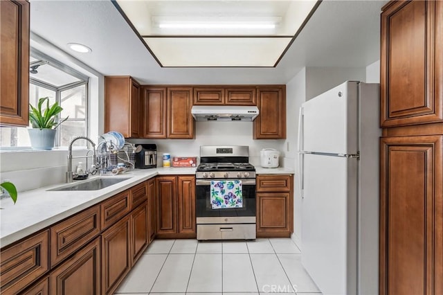 kitchen with freestanding refrigerator, under cabinet range hood, light tile patterned floors, a sink, and stainless steel range with gas cooktop