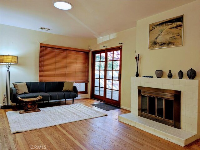 living room featuring a brick fireplace, baseboards, visible vents, and wood finished floors
