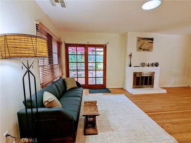 living area featuring baseboards, a brick fireplace, wood finished floors, and visible vents