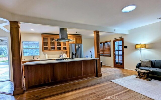kitchen featuring stainless steel appliances, ornate columns, island exhaust hood, and glass insert cabinets