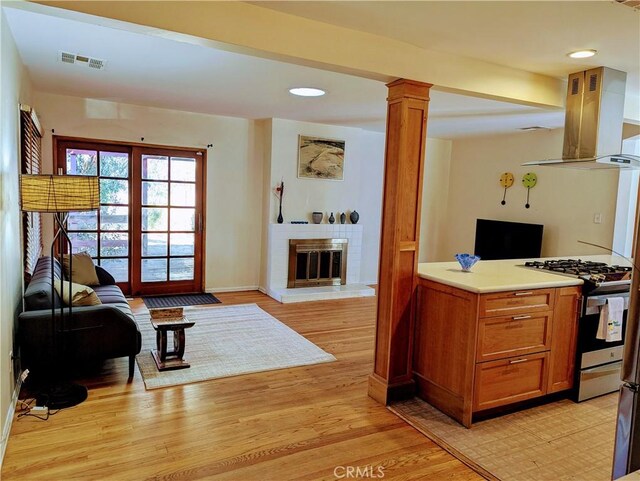 interior space with visible vents, a brick fireplace, baseboards, light wood-style floors, and ornate columns