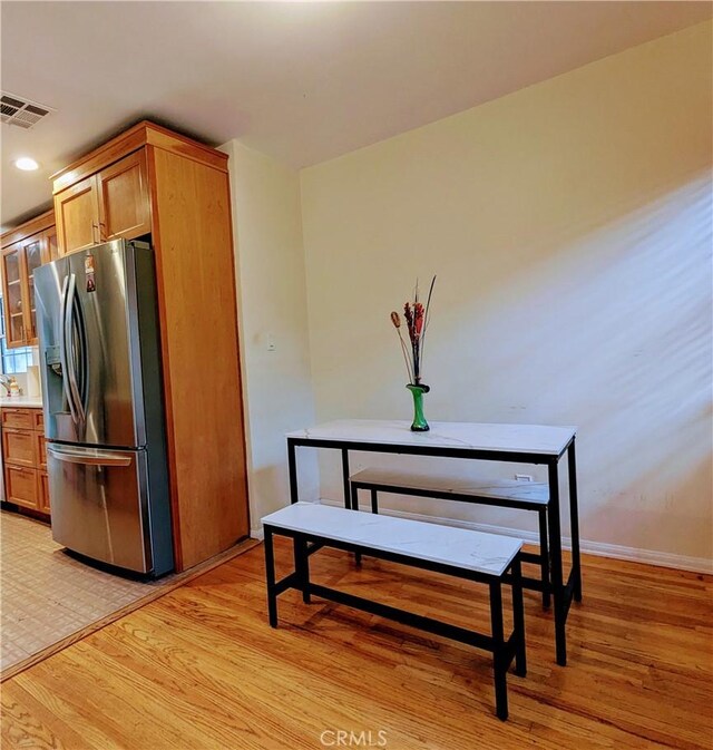 interior space with stainless steel fridge with ice dispenser, baseboards, light wood-style flooring, and visible vents
