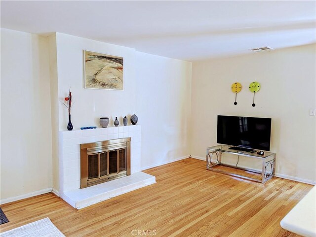 living area with visible vents, baseboards, a glass covered fireplace, and wood finished floors
