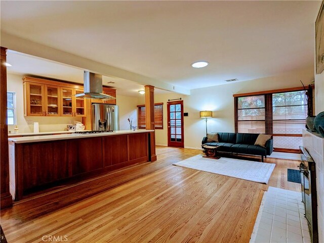 living area featuring ornate columns, light wood-style flooring, a wealth of natural light, and visible vents