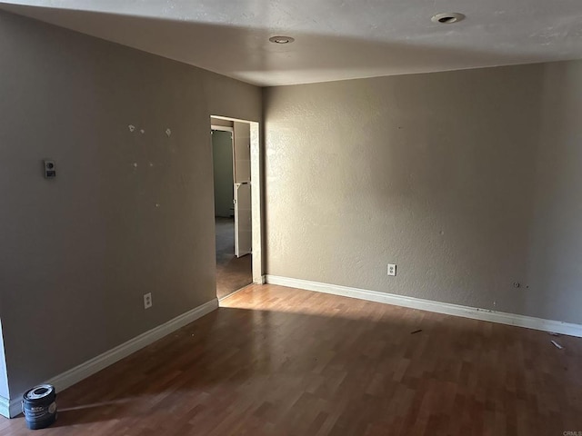 unfurnished room featuring baseboards, a textured wall, and wood finished floors