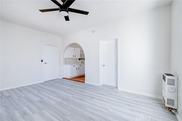 empty room with baseboards, ceiling fan, heating unit, and light wood-style flooring