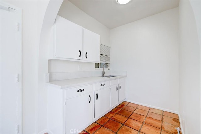 kitchen with arched walkways, a sink, light countertops, baseboards, and white cabinets