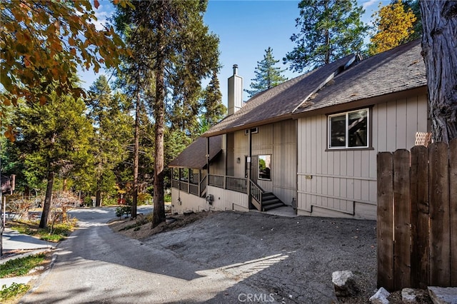 view of home's exterior with roof with shingles, fence, and a chimney