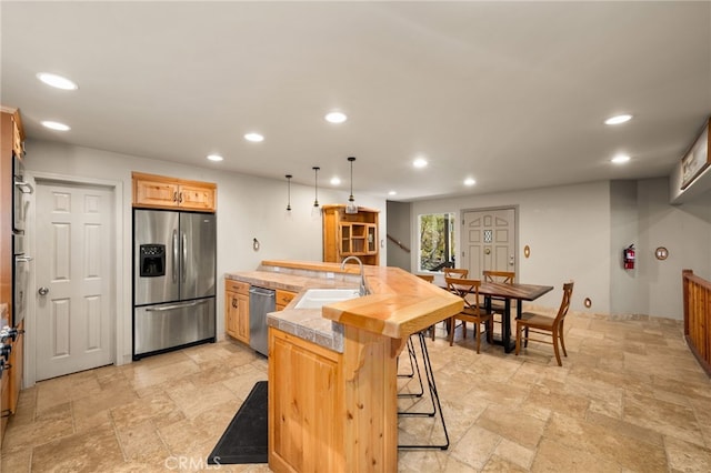 kitchen featuring a sink, a breakfast bar area, stone tile floors, stainless steel appliances, and recessed lighting