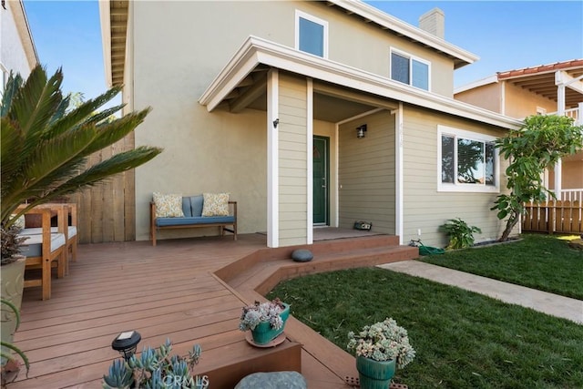 rear view of property with fence, stucco siding, a deck, a chimney, and a yard