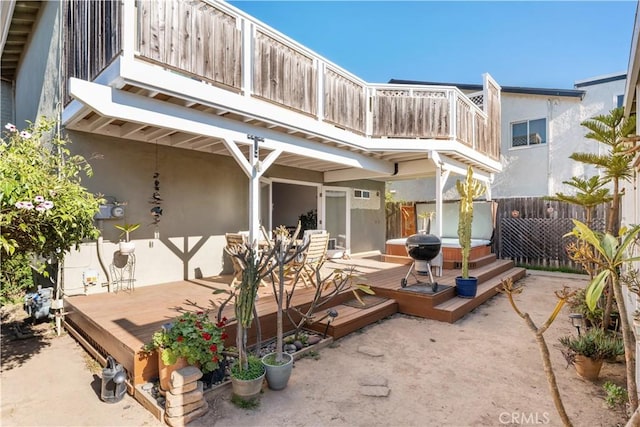 back of property featuring fence, a balcony, a deck, stucco siding, and a hot tub