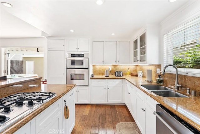 kitchen with appliances with stainless steel finishes, a sink, light wood finished floors, white cabinetry, and glass insert cabinets