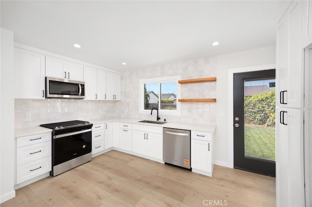kitchen featuring appliances with stainless steel finishes, tasteful backsplash, a sink, light countertops, and light wood-style floors
